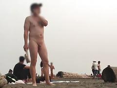As mulheres vestidas passam por um homem nu com um pequeno pau na praia